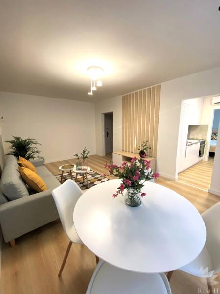 Ebédlő egy kétszobás lakásban, fehér asztallal és fa mintázatú padlóval.