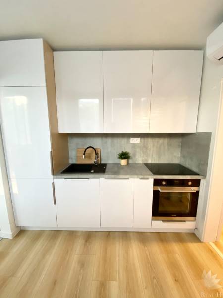 Konyha fehér szekrényekkel, szürke munkalappal és fa mintázatú padlóval, 2 szobás lakás.