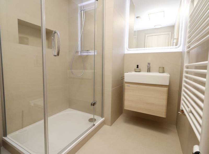 Fürdőszoba üveg zuhanykabinnal és világos mosdóval egy kétszobás lakásban.