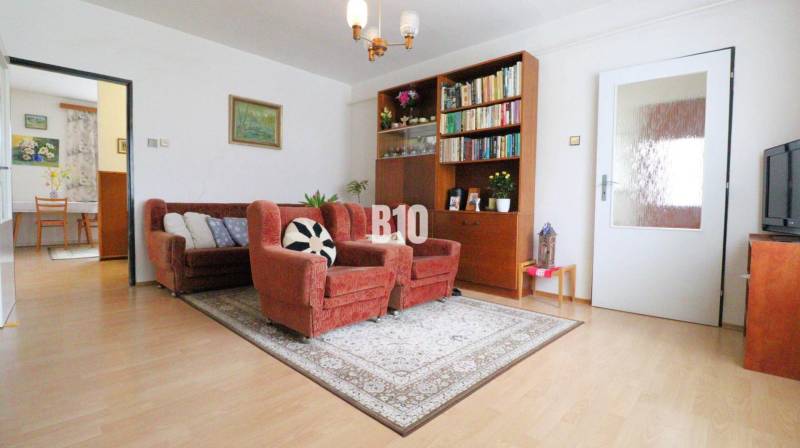 Családi ház nappalija kanapéval, fotelekkel és könyvespolccal, fa dekorációjú padlón.