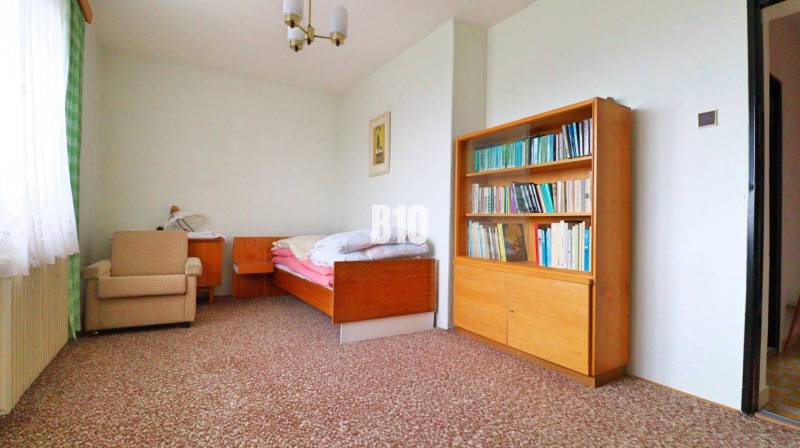 Szoba családi házban ággyal, könyvespolccal és szőnyegen lévő fotellel.