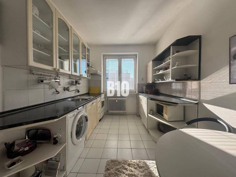 Konyha egy kétszobás lakásban fehér szekrényekkel és fekete munkalappal.