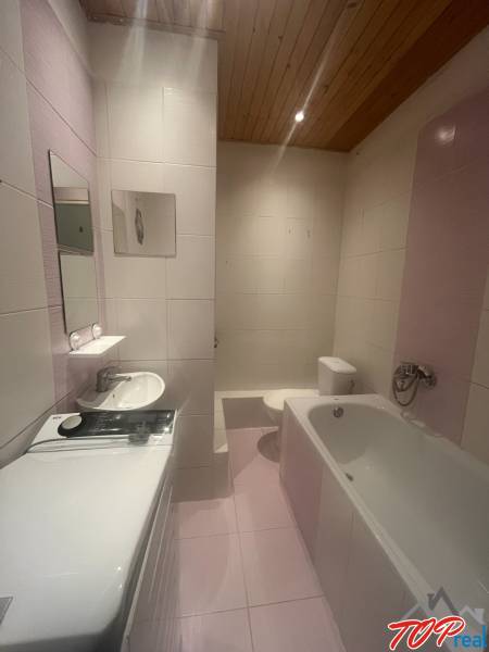 Fürdőszoba garzonlakásban káddal, mosógéppel, mosdóval és WC-vel.