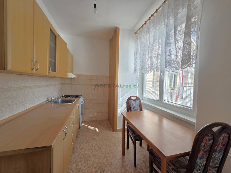 Konyha fa szekrényekkel, asztallal és két székkel egy háromszobás lakásban.