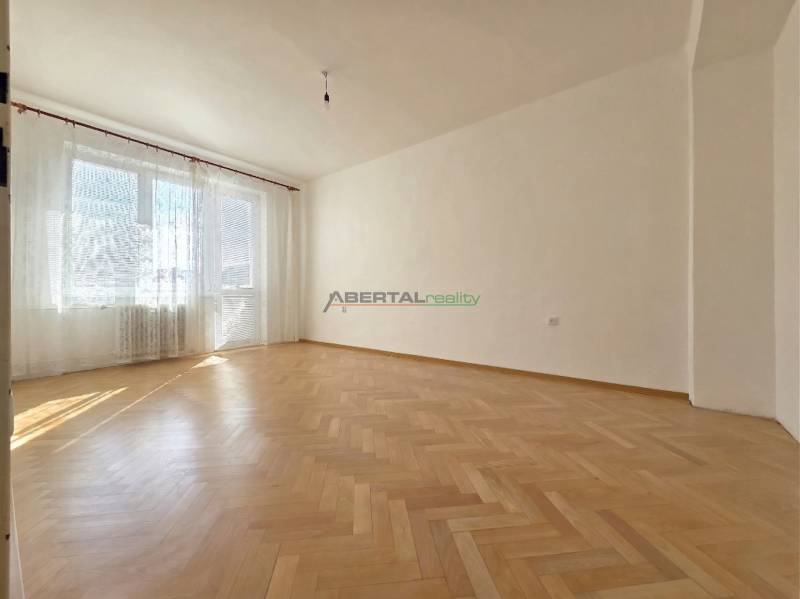 Tágas szoba nagy ablakokkal és fa dekorációjú padlóval egy háromszobás lakásban.