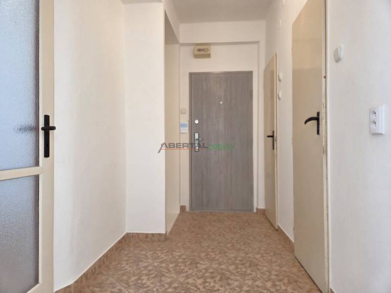 Folyosó csempével, fehér falak és több ajtó egy háromszobás lakásban.