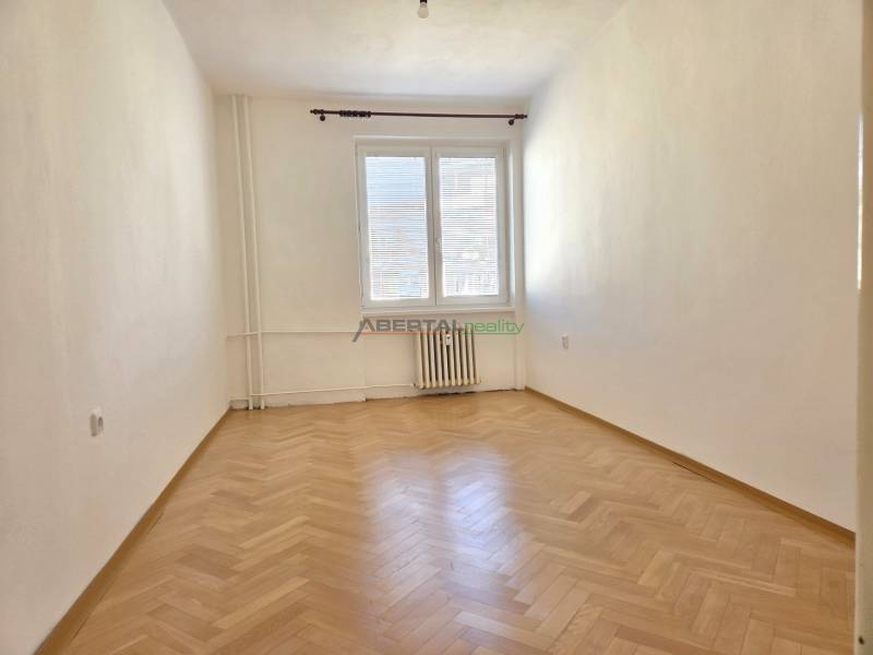 Üres szoba fa dekorációjú padlóval egy háromszobás lakásban, világos falak, radiátor.