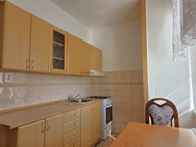 Konyha világos bútorokkal, tűzhellyel és asztallal egy háromszobás lakásban.