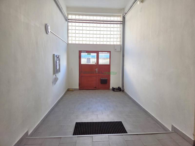 Folyosó csempével, amely a háromszobás lakás piros ajtajához vezet.