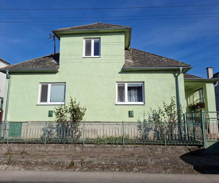 Családi ház Kisleváron világoszöld homlokzattal és meredek tetővel.