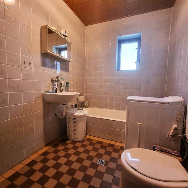 Fürdőszoba családi házban káddal, mosdóval és mosógéppel, sakktáblás csempével.