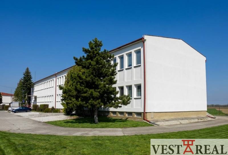 Egy épület Sopornyán, amelyet zöld növényzet és fák vesznek körül, tiszta kék égbolttal.