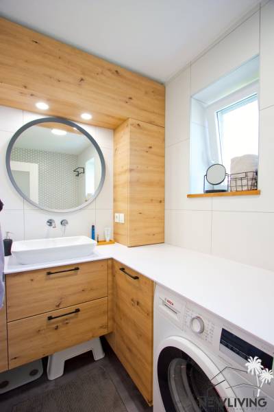 Fürdőszoba egy háromszobás lakásban kerek tükörrel és fa részletekkel.