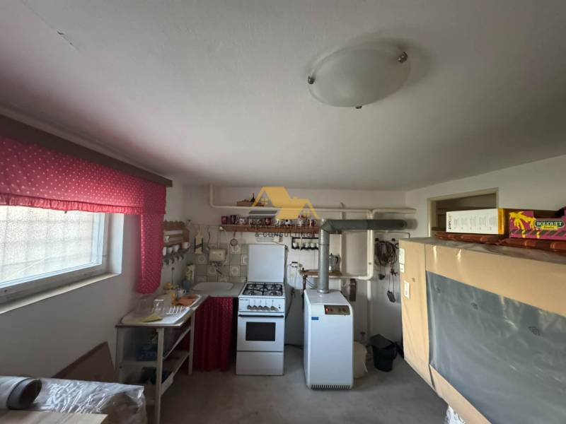 Családi ház konyhája régebbi tűzhellyel és élénkvörös függönyökkel.