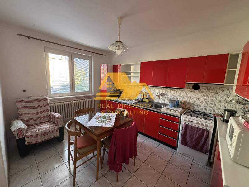 Konyha piros konyhabútorral egy családi házban, asztallal és székkel felszerelve.