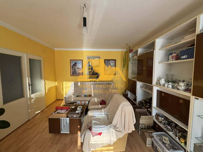 Nappali egy családi házban fehér kanapéval, fa mintázatú padlóval, sárga falakkal.