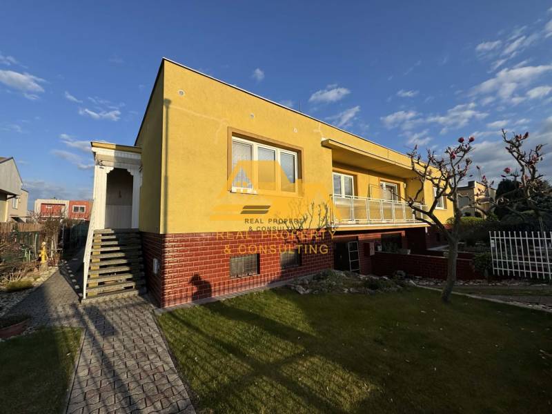 Sárga családi ház Érsekújváron, rendezett kerttel és járdával az utcán.