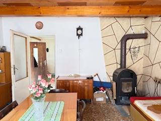 Családi ház belső tere cserépkályhával, fából készült mennyezettel és virágokkal díszített étkezőasztallal.