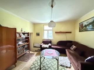 Nappali szőnyegekkel, könyvekkel, barna kanapéval és fa dekorációjú padlóval egy családi házban.