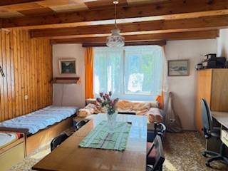 Izba egy családi házban fa gerendákkal, étkezőasztallal és két ággyal.