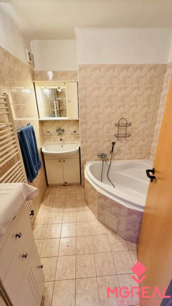 A háromszobás lakás fürdőszobája káddal, mosdóval és bézs csempékkel.