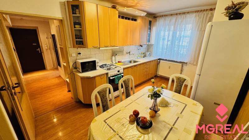 Konyha egy háromszobás lakásban, fa dekor padlóval és étkezőasztallal.