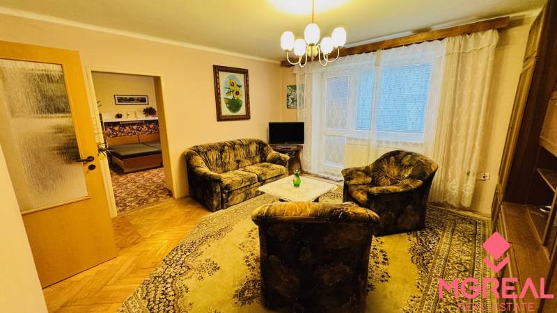 Nappali egy háromszobás lakásban kanapéval, fotellel és fa dekorációjú padlóval.