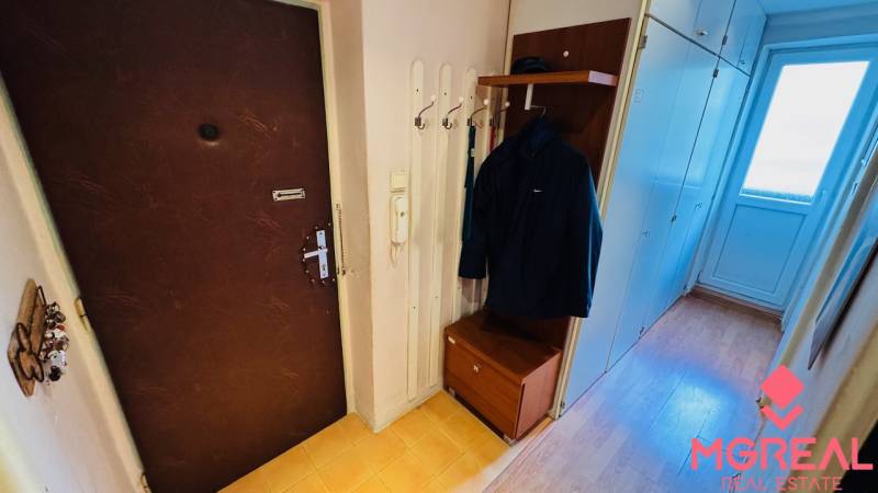 Előszoba fogassal, szekrénnyel és fa dekorációjú padlóval egy háromszobás lakásban.