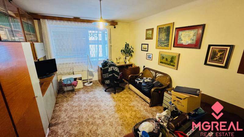 Nappali egy háromszobás lakásban dekorációkkal, bútorokkal és fa mintázatú padlóval.