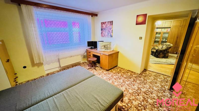 Szoba egy háromszobás lakásban szőnyeggel, íróasztallal és ággyal.