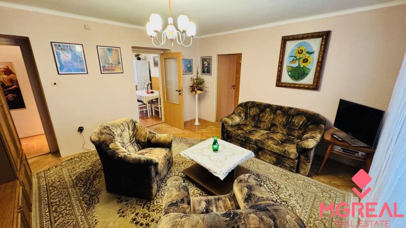 Nappali szoba fotelekkel, kanapéval és szőnyeggel egy háromszobás lakásban.