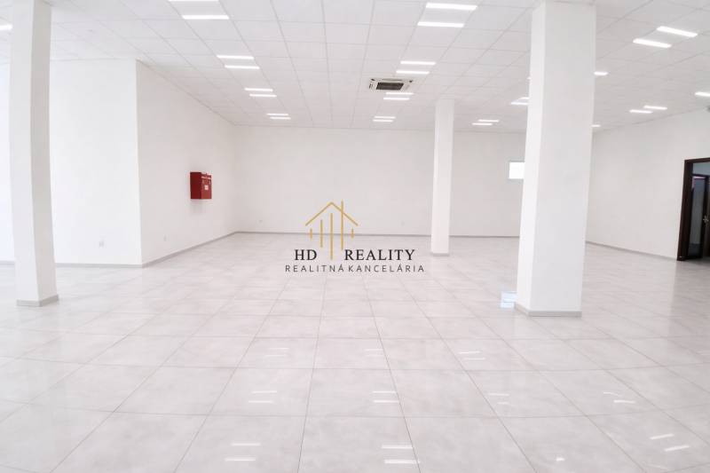 Tágas üzlethelyiségek fehér padlóval és oszlopokkal, világos világítással.