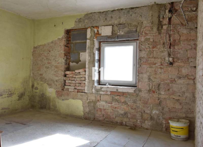 Szoba egy családi házban téglafalakkal és egy vödörrel a padlón.