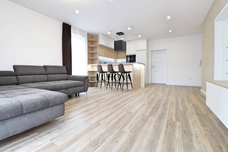 Nappali egy háromszobás lakásban kanapéval, bárral és fa dekorációjú padlóval.