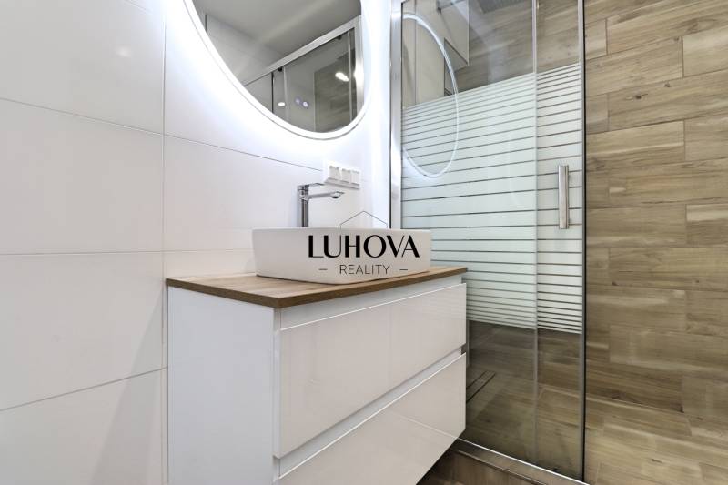 Fürdőszoba mosdóval és zuhanyzóval egy háromszobás lakásban, fa dekoros padlóval.