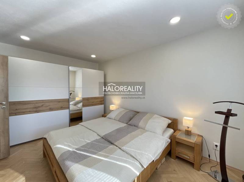 Világos hálószoba egy egyszobás lakásban, fa dekor padlóval és beépített szekrénnyel.