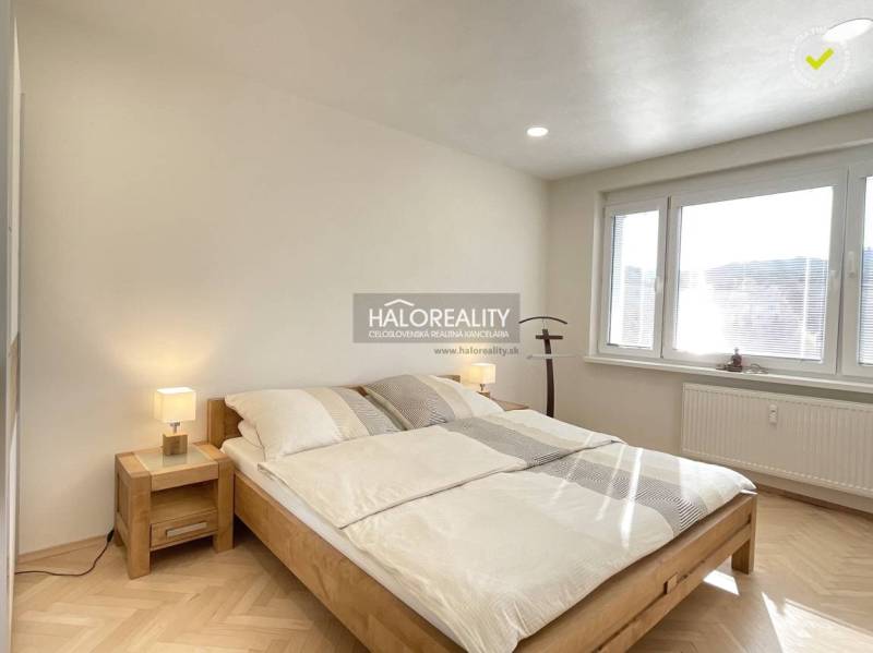 Világos hálószoba egy egyszobás lakásban, fa dekoros padlóval és nagy ablakkal.