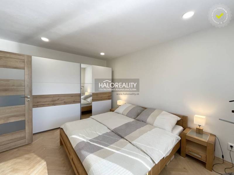 Hálószoba fa mintázatú padlóval egy egyszobás lakásban, világos ágy és szekrény.