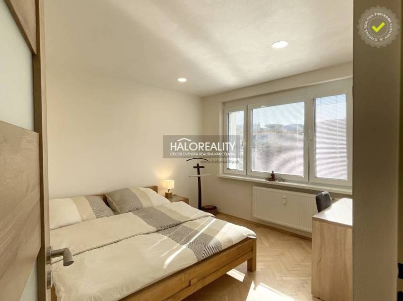 Hálószoba egy egyszobás lakásban fa mintázatú padlóval és nagy ablakokkal.