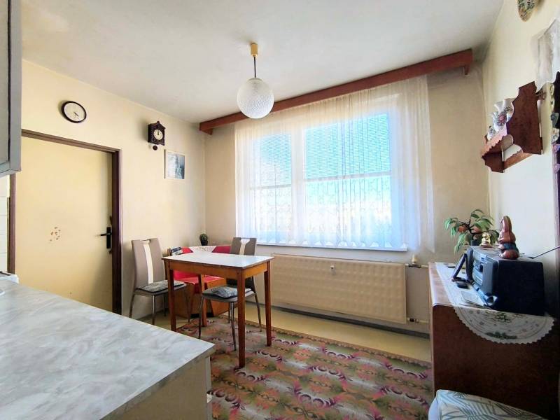 Ebédlő egyszerű bútorokkal egy háromszobás lakásban, padló dekoratív szőnyeggel.