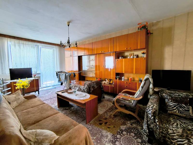 Nappali egy háromszobás lakásban rusztikus bútorokkal és feltűnő szőnyeggel.