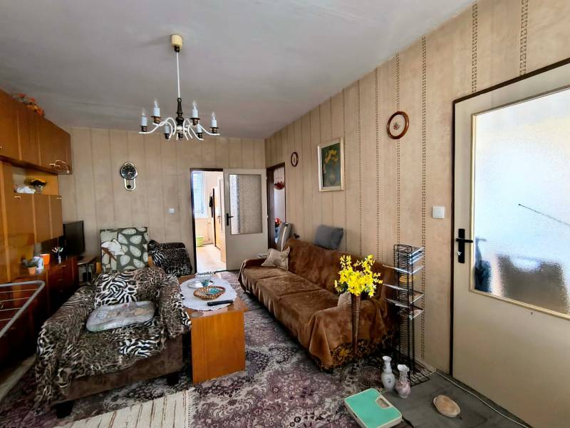 Nappali egy háromszobás lakásban, fotelekkel, virágokkal és vintage csillárral.