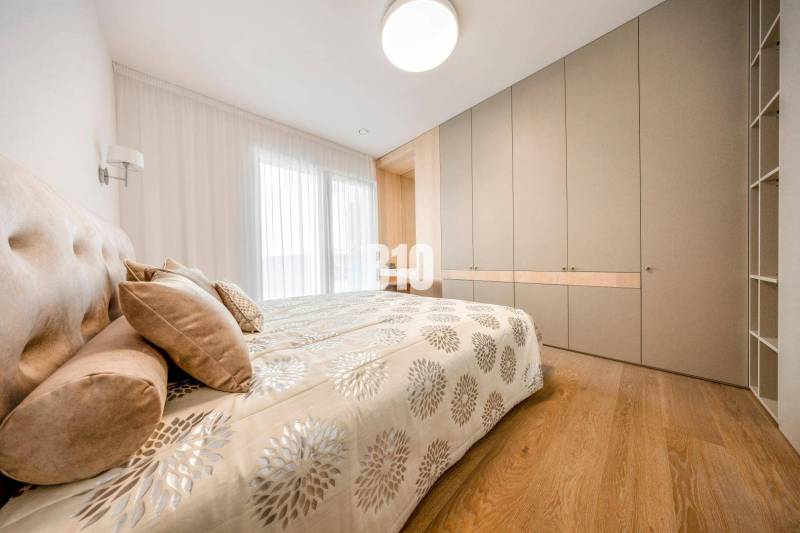 Hálószoba egy háromszobás lakásban ággyal, beépített szekrénnyel és fa dekorációjú padlóval.