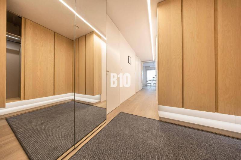 Folyosó egy 3 szobás lakásban fa mintázatú padlóval és tükörrel.