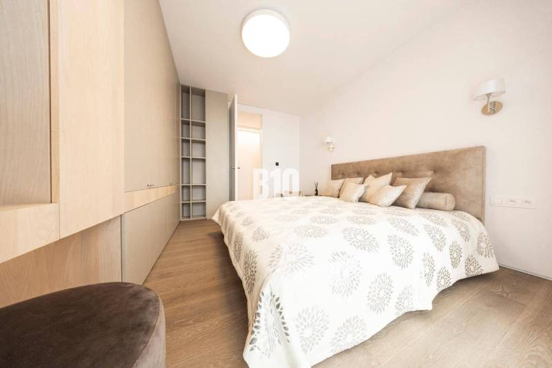 Világos hálószoba fa hatású padlóval és beépített szekrényekkel egy háromszobás lakásban.