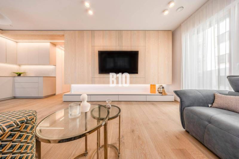 Nappali egy háromszobás lakásban, fa dekoros padlóval és falra szerelt televízióval.