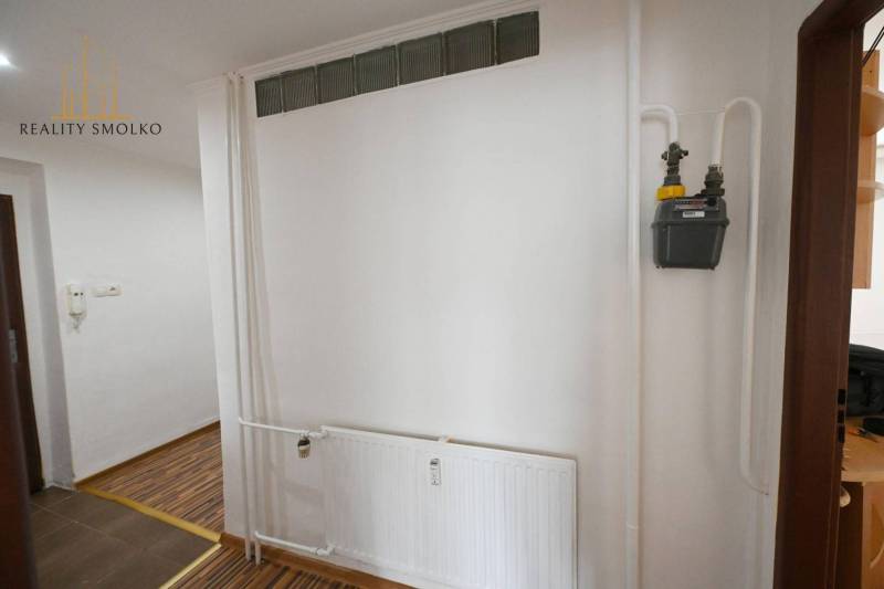 Belső tér fehér fallal, radiátorral és fa dekorációjú padlóval egy kétszobás lakásban.