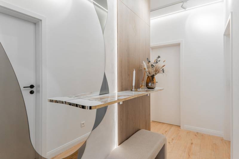 Folyosó egy 3 szobás lakásban minimalista asztallal, tükörrel és fa dekoros padlóval.