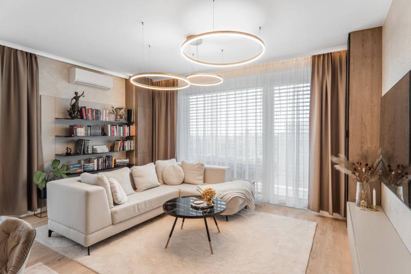 Nappali szoba fa dekor padlóval egy háromszobás lakásban, kényelmes kanapé, könyvtár.