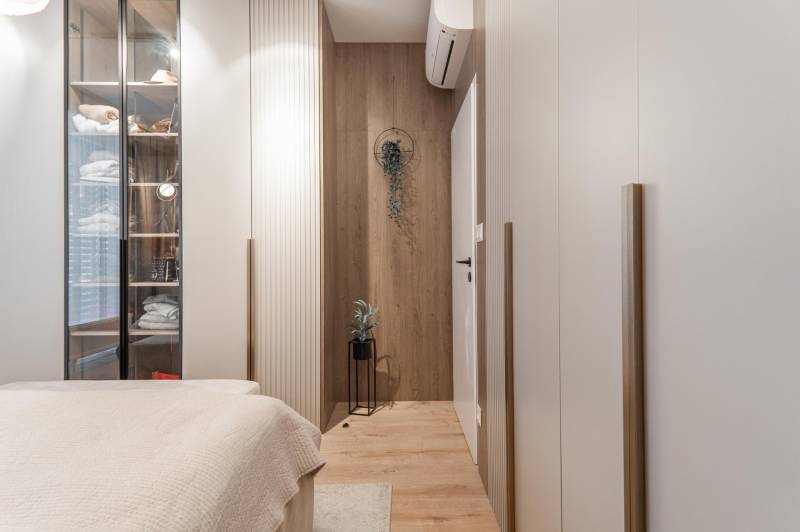 Hangulatos hálószoba fa dekor padlóval és üvegszekrénnyel egy háromszobás lakásban.